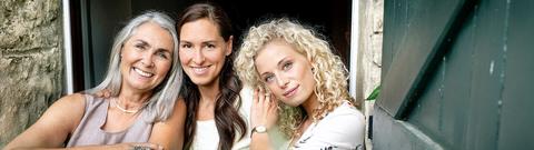 Drei Frauen blicken lächelnd in die Kamera